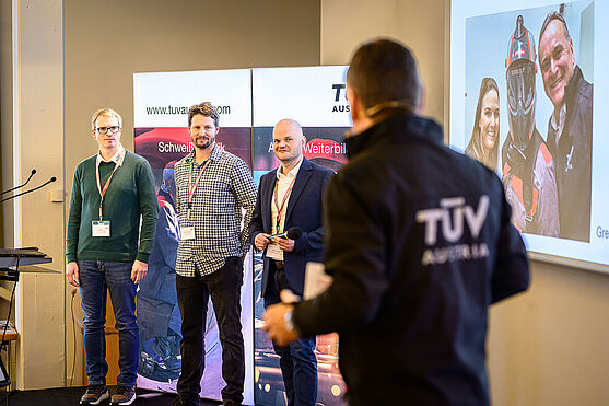 Eben noch in Wien, jetzt auf der Showbühne: Die Experten erklärten auch vor Ort, wie Werkstoffe reagieren, wenn das Thermometer verrückt spielt.<br /> 3 Männer stehen auf einer Bühne. Mit dem Rücken zur Kamera steht ein vierter Mann mit 'TÜV AUSTRIA Jacke. Die Männer reden miteinander.
