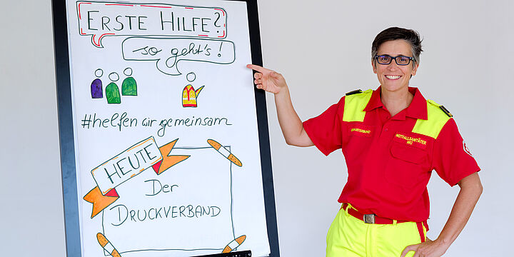 Sanitäterin vor einem Whiteboard mit Infos zum Thema Erste Hilfe.