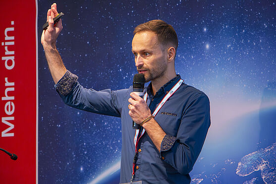 Patrick Pammer (Preductive Digital Services GmbH) mit dem Vortrag Duale Ausbildung für Schweißer/innen: Virtuelle Schweißtechnologien im Einsatz<br /> Mann mit Mikrofon auf der Bühne.