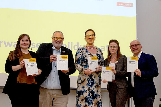 Gruppe bisheriger Autor:innen aus der TÜV AUSTRIA Akademie<br /> Gruppenfoto vor Leinwand