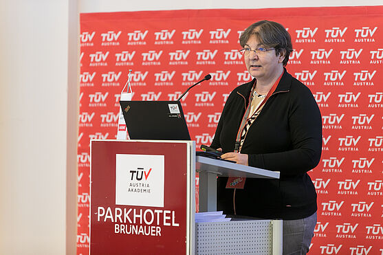 Dame steht hinter Rednerpult und hält Vortrag.