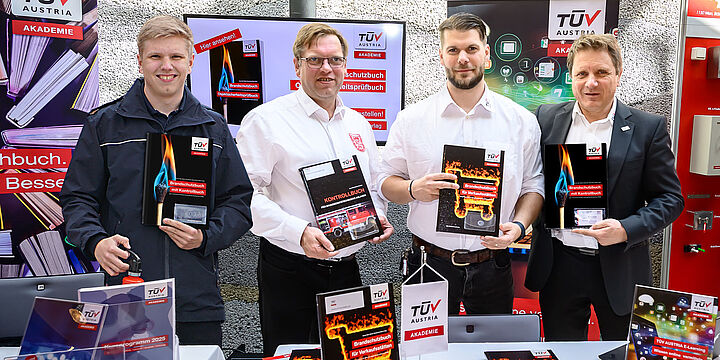 4 Männer stehen hinter einem Ausstellertisch und halten das neue Brandschutzbuch in die Kamera
