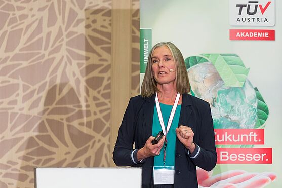 Die erste Vortragende des Tages: Mira Maria Meiler von essence consulting. Sie sprach über die pragmatische Umsetzung von Nachhaltigkeit<br /> Mira Maria Meiler von essence consulting. Eine Frau in Business Kleidung hinter einem Referentenpult. Sie spricht im Vortrag über die pragmatische Umsetzung von Nachhaltigkeit