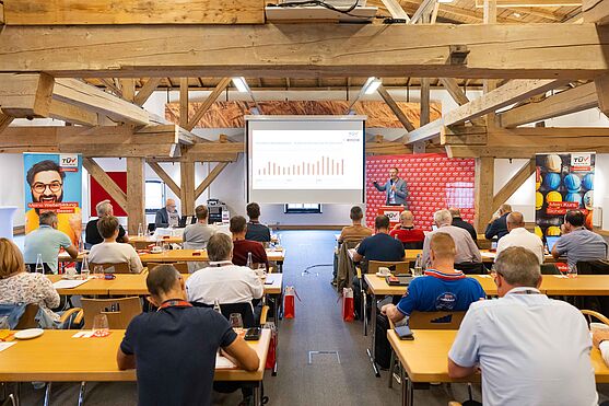 Martin Schmutzer (TÜV AUSTRIA Akademie) hieß die Teilnehmenden herzlich willkommen zum TÜV AUSTRIA Sicherheitstag in der ehemaligen Malztenne.<br /> Man hinter Rednerpult hält Moderationskarten und lächelt.