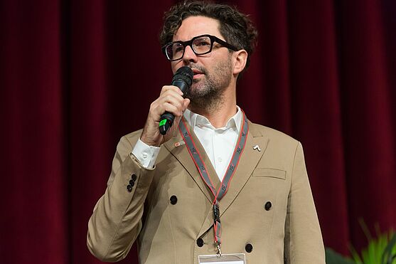 Auch von Michael Kienesberger, Stadt Wien-Umweltschutz gab es eine kurze Ansprache, bevor es mit den ersten Vorträgen des Tages losging.<br /> Mann mit Brille spricht auf Bühne in ein Mikrofon.