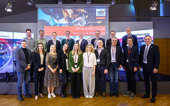 In der Pause war Zeit für ein Gruppenfoto mit den Referent:innen.<br /> Eine gemischte Frauen- und Männergruppe in Businessoutfits steht vor einer Leinwand mit der Aufschrift: Tag der Schweiß- und Prüftechnik. Sie lächeln in die Kamera.
