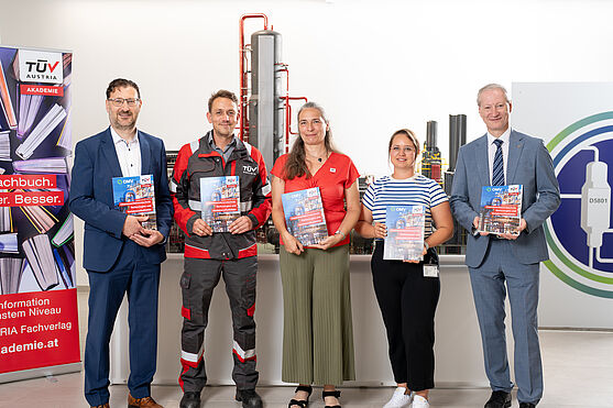 5 Menschen stehen vor dem Modell der Raffinerie Schwechat und haben das Buch Chemieverfahrenstechnik in der Hand