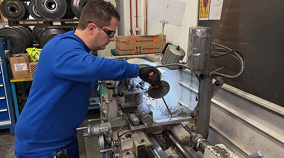 Ein Mann zeigt vor einer Maschine das Entfernen von Metallspänen mit passendem Werkzeug vor