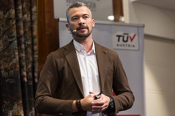 Michael Kazianschütz vom LKH-Univ. Klinikum Graz (KAGes) sprach über Lean Logistik: Mit Lean-Prinzipien Prozesse optimieren.<br /> Vortragender mit Bart, Hemd und Sakko auf der Bühne.