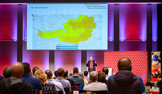 Mann auf Bühne hält Präsentation vor Publikum.