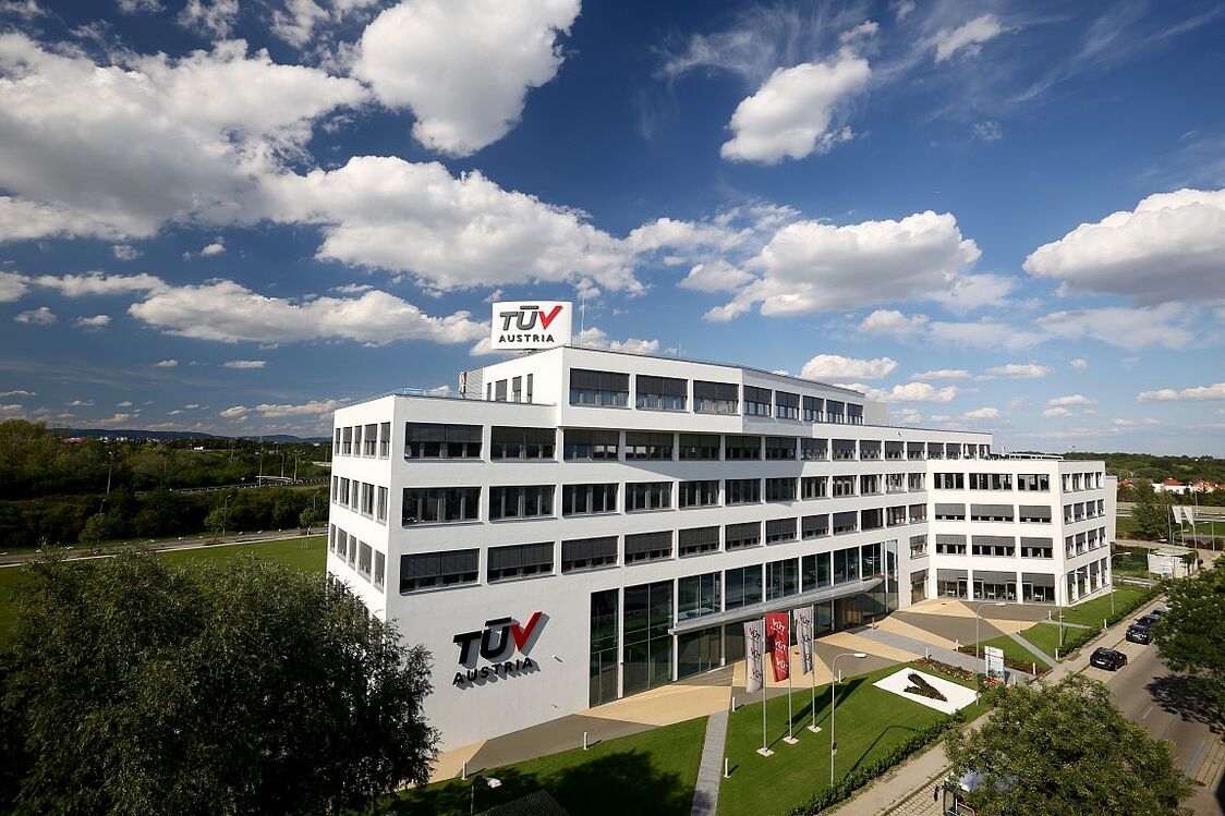 TÜV AUSTRIA Gebäude in Brunn am Gebirge<br /> Ein modernes, mehrstöckiges Bürogebäude aus der Vogelperspektive mit blauem Himmel und vereinzelten Wolken.