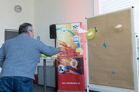 Mann wirft Papierflieger in Richtung eines Luftballons.