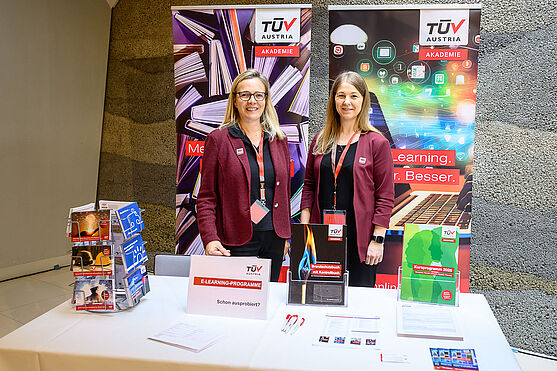 Zwei freundlich lächelnde Damen an einem Infostand.