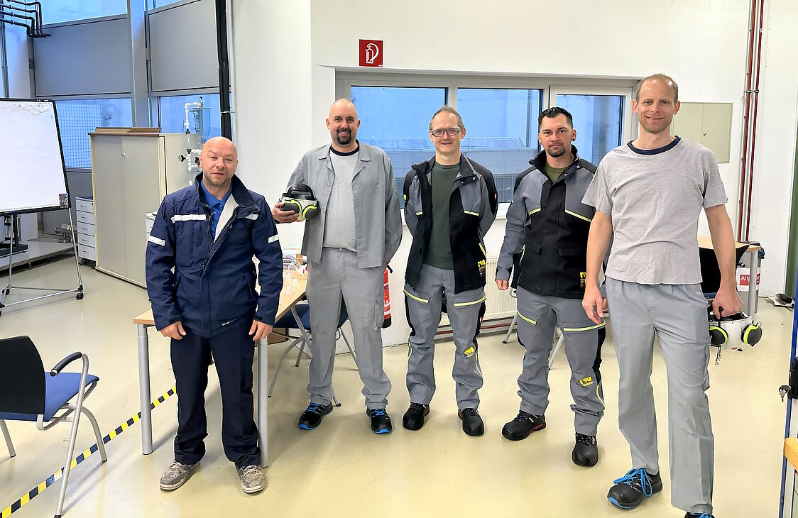 <br /> Fünf freundlich lächelnde Herren in Arbeitskleidung.