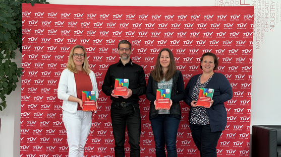 4 Personen, 3 Frauen und 1 Mann, stehen vor einer roten Logowand und halten das Cover des neuen Buches in die Kamera