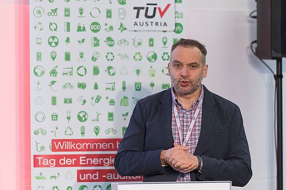 Mann steht hinter Rednerpult und hält Vortrag.