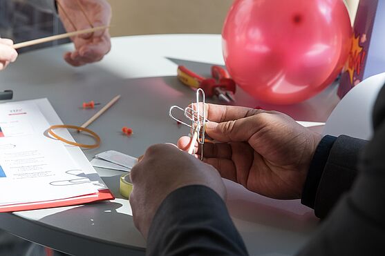 Mann bastelt etwas mit mehreren Büroklammern. Im Hintergrund ein Ballon.