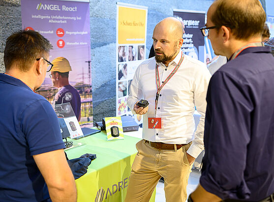 Drei Männer sprechen miteinander. Im Hintergrund ein Ausstellerstand.