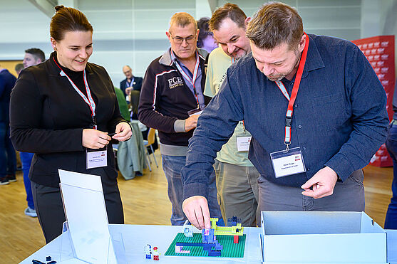 ...und Technik zum anfassen.<br /> 3 Männer und eine Frau basteln an einer Lego-Baustelle, die auf einem Tisch steht.