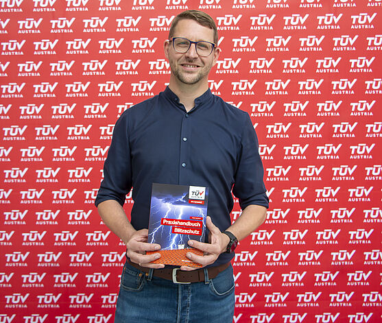 Ein Mann, Autor Peter Schiffner, steht mit dem neuen Praxishandbuch Blitzschutz vor einer roten Pressewand