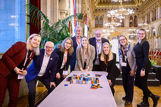 Menschen stehen um einen Tisch auf dem Dominosteine aufgestellt sind.