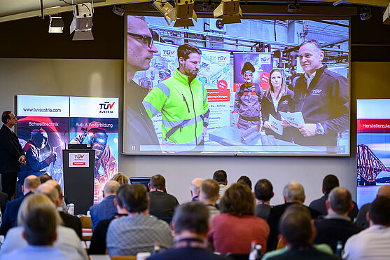 Schweißen unter Extrembedingungen. Das zeigten Martin Willinger (Fronius International GmbH), Michael Jagschitz & Andreas Polt (TÜV AUSTRIA GMBH) in der Umweltsimulationskammer des Prüfzentrums.<br /> Leute im Saal sehen sich auf der Bühne das Video auf der Leinwand an. Zu sehen sind 5 Menschen, die sich unterhalten.