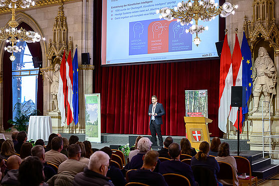 Mann auf Bühne hält Vortrag.