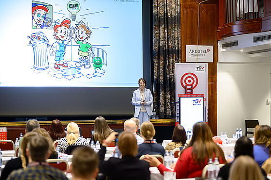 Dame auf der Bühne hält Vortrag.