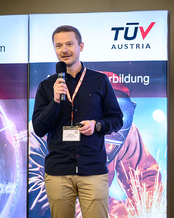 Last but not least lieferte Dominik Haas (OMV Downstream GmbH) spannende Einblicke in die Reparatur der Rohöldestillationskolonne 2022 OMV Raffinerie Schwechat.<br /> Ein Mann mit kurzen, dunklen Haaren spricht in ein Mikro.