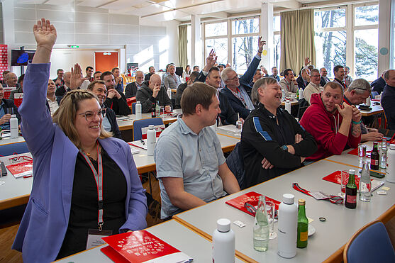 Publikum während eines Vortrags. Einige Personen heben die Hand.
