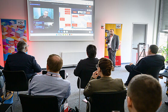 Mann ist auf Leinwand zu sehen und hält via Online-Zuschaltung Vortrag.