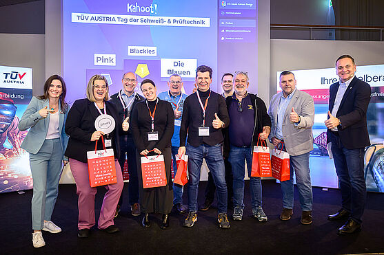Die glücklichen Gewinner:innen wurden rasch gefunden, beschenkt und bejubelt.<br /> Eine Gruppe von Männern und Frauen mit Goodiebags des TÜV AUSTRIA lächeln in die Kamera. Einige haben das Daumen-hoch Zeichen geformt.