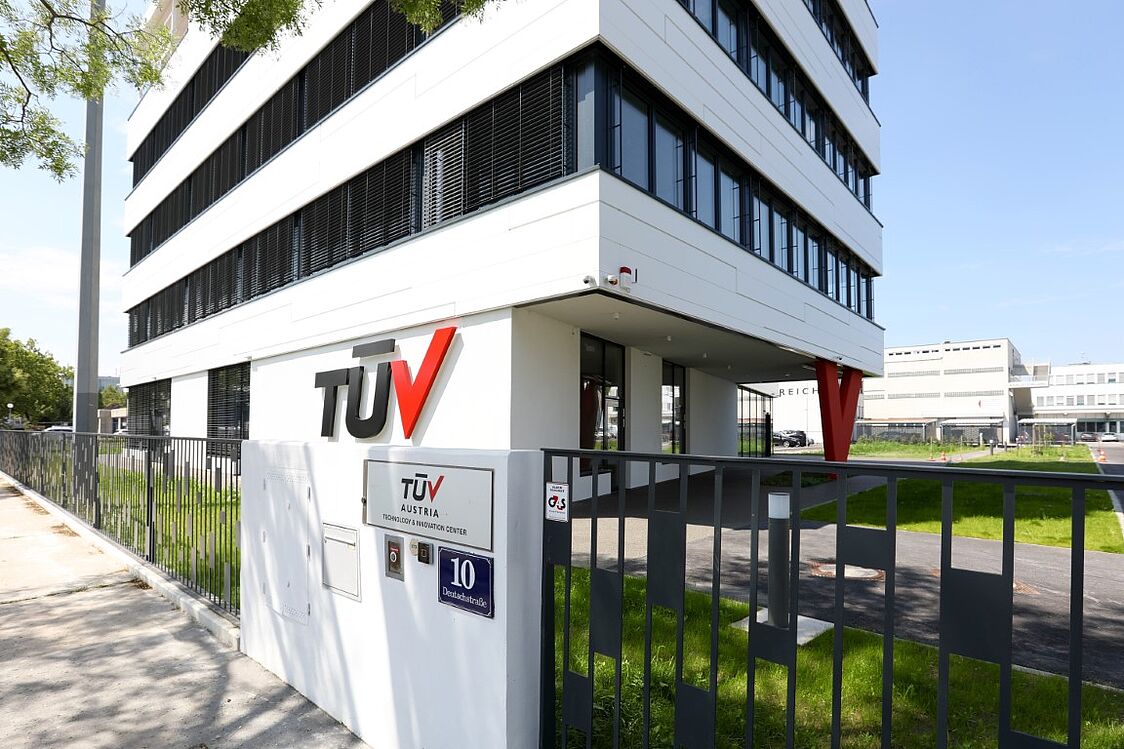 Ein modernes, mehrstöckiges Bürogebäude von außen mit dem Logo des TÜV AUSTRIA an der Fassade 