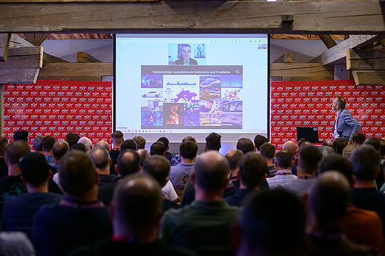 Herbert Saurugg, MSc (Blackout und Krisenvorsorge) per Live-Zuschaltung mit einer spannenden Keynote: Vom Blackout zum Notfall: Praxisszenarien und Notfallplanung im Brandschutz.<br /> Mann hält Präsentation per Onlinezuschaltung. Er ist gemeinsam mit seiner Präsentation auf der Leinwand zu sehen.