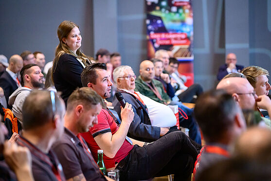 Mann aus dem Publikum spricht in ein Mikrofon.