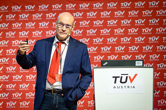 Mann steht neben Rednerpult und hält Präsenter in der Hand.