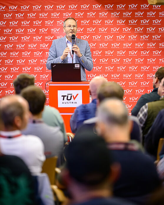 Martin Schmutzer (TÜV AUSTRIA Akademie) begrüßte die Teilnehmer:innen und hieß sie herzlich willkommen zum TÜV AUSTRIA Brandschutztag.<br /> Mann spricht in Handmikrofon.
