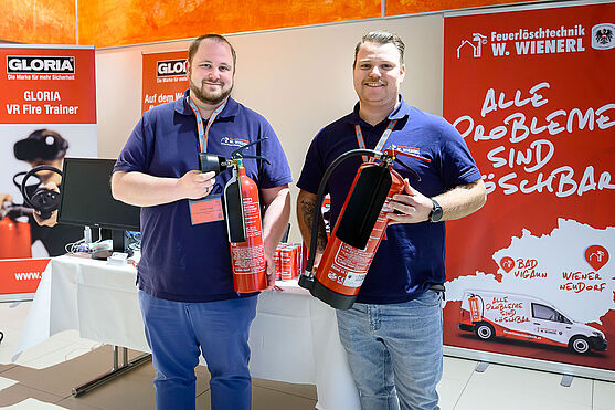 Zwei lächelnde Männer halten jeweils einen Feuerlöscher in der Hand.