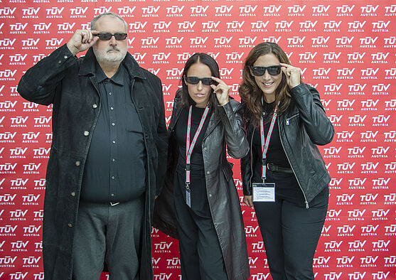 <br /> Gruppenfoto: Zwei Damen und ein Herr. Jeweils schwarz gekleidet und mit Sonnenbrille
