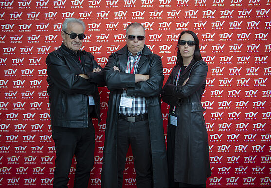 <br /> Gruppenfoto: Zwei Herren und eine Dame. Jeweils schwarz gekleidet und mit Sonnenbrille