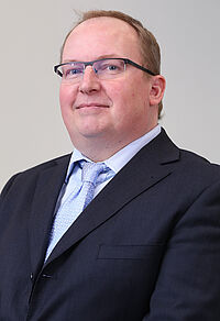 Mann im Anzug lächelt freundlich.
