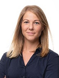 Bianca Rupsch, eine Frau in einer blauen Bluse, posiert lächelnd vor einem neutralen Hintergrund.