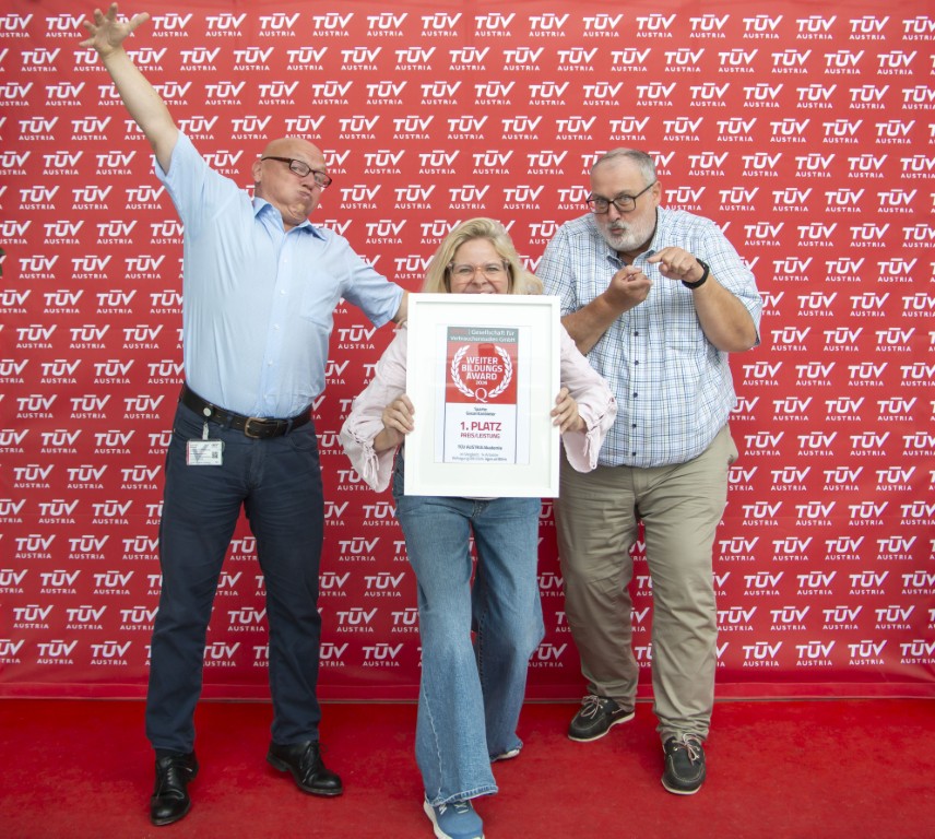Viel wert zum fairen Preis: Christian Bayer, Nina Munk und Thomas Rochowansky freuen sich über den 1. Platz für Preis-Leistungs-Verhältnis<br /> Christian Bayer, Nina Munk und Thomas Rochowansky stehen vor einer Pressewand. Nina Munk hält das Zertifikat in die Kamera. Christian Bayer hat beide Arme weit ausgebreitet - großer Wert. Thomas Rochowansky zeigt mit Daumen und Zeigefingern den kleinen Preis an.